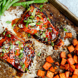 Two fillets of salmon on a sheet pan with veggies.
