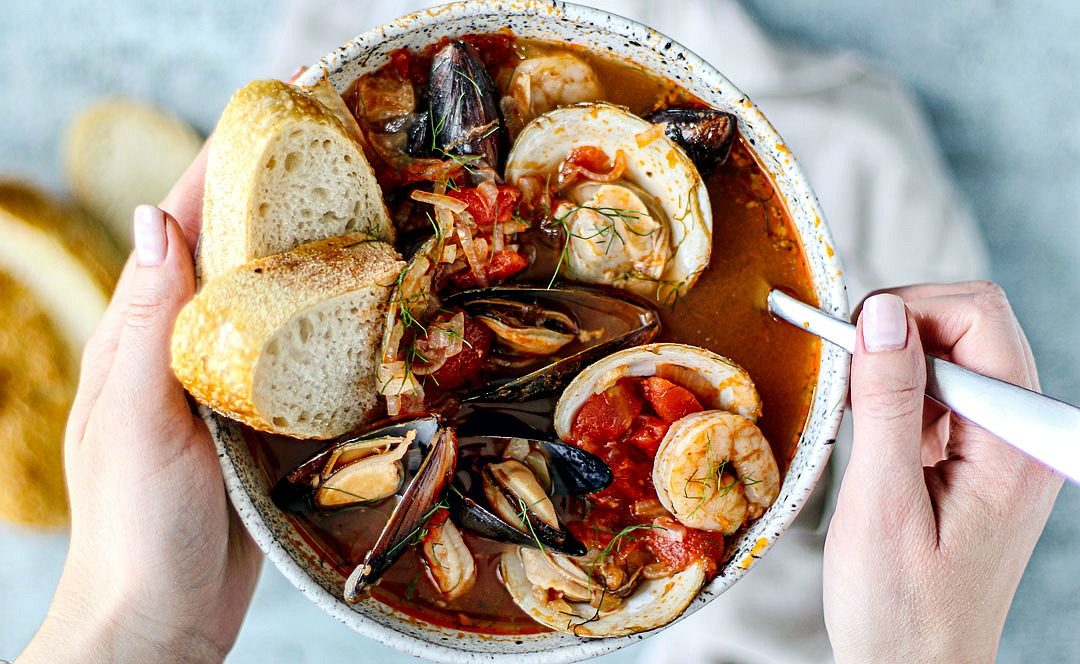 Hands holding bowl of cioppino.