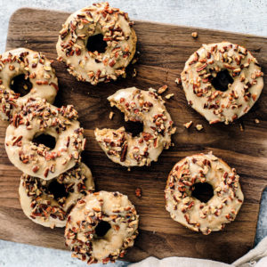 Wooden board full of maple baked donuts with pecans on top.