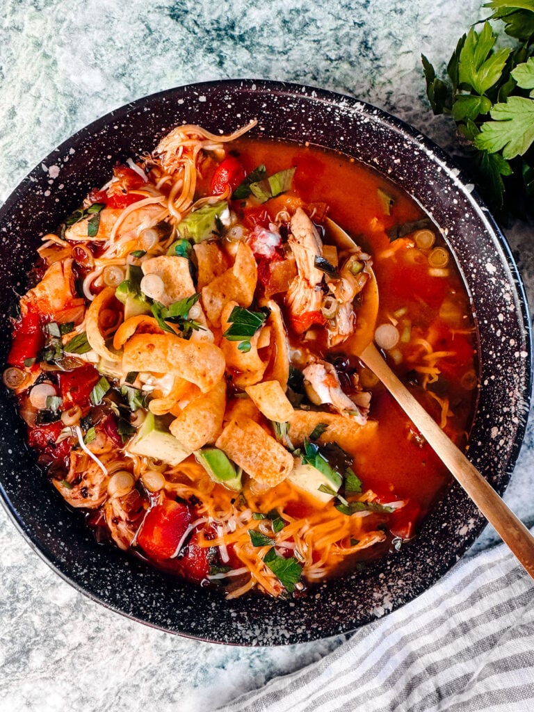Bowl of chicken tortilla soup topped with corn chips, avocado, and parsley.