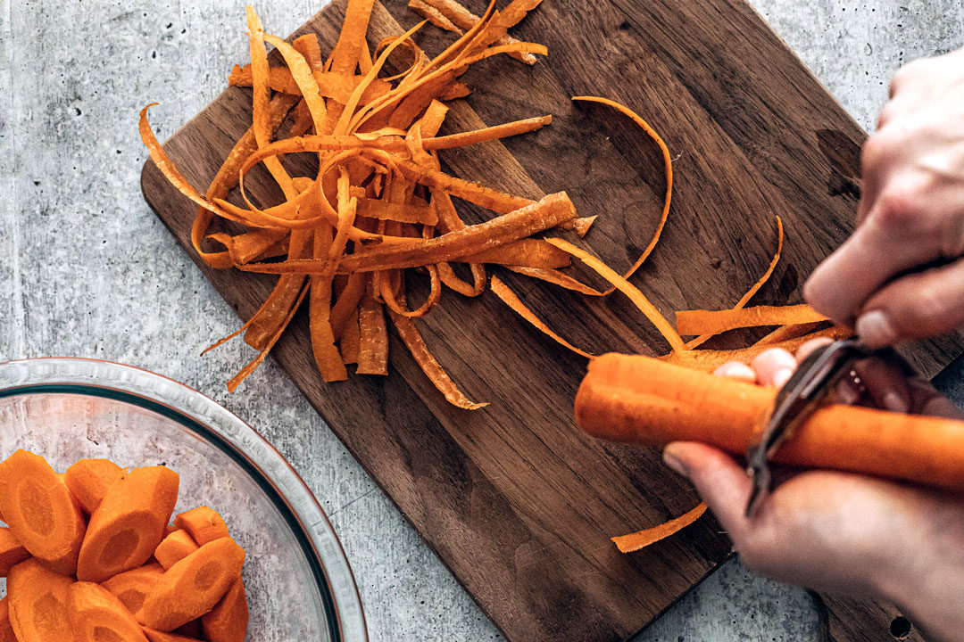 Hand peeling carrot with ribboned carrot shavings.