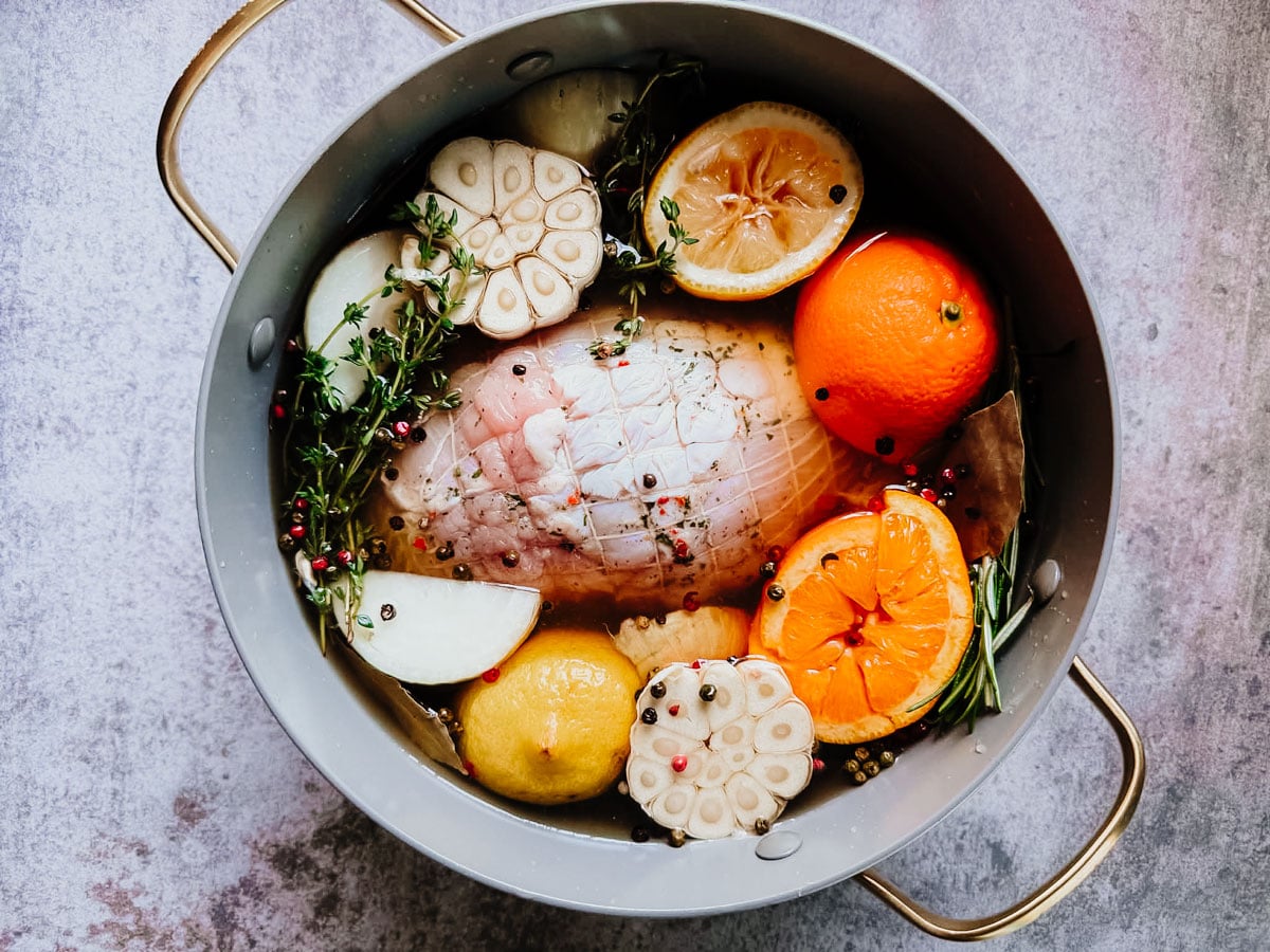 Turkey breast in pot of brine with citrus fruits, herbs, garlic, and spices.