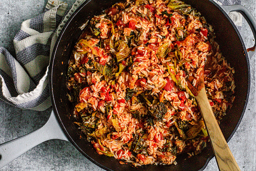 Pan of unstuffed cabbage rolls with wooden spoon.