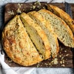 Sliced loaf of homemade bread with roasted garlic and rosemary, sliced on a cutting board.
