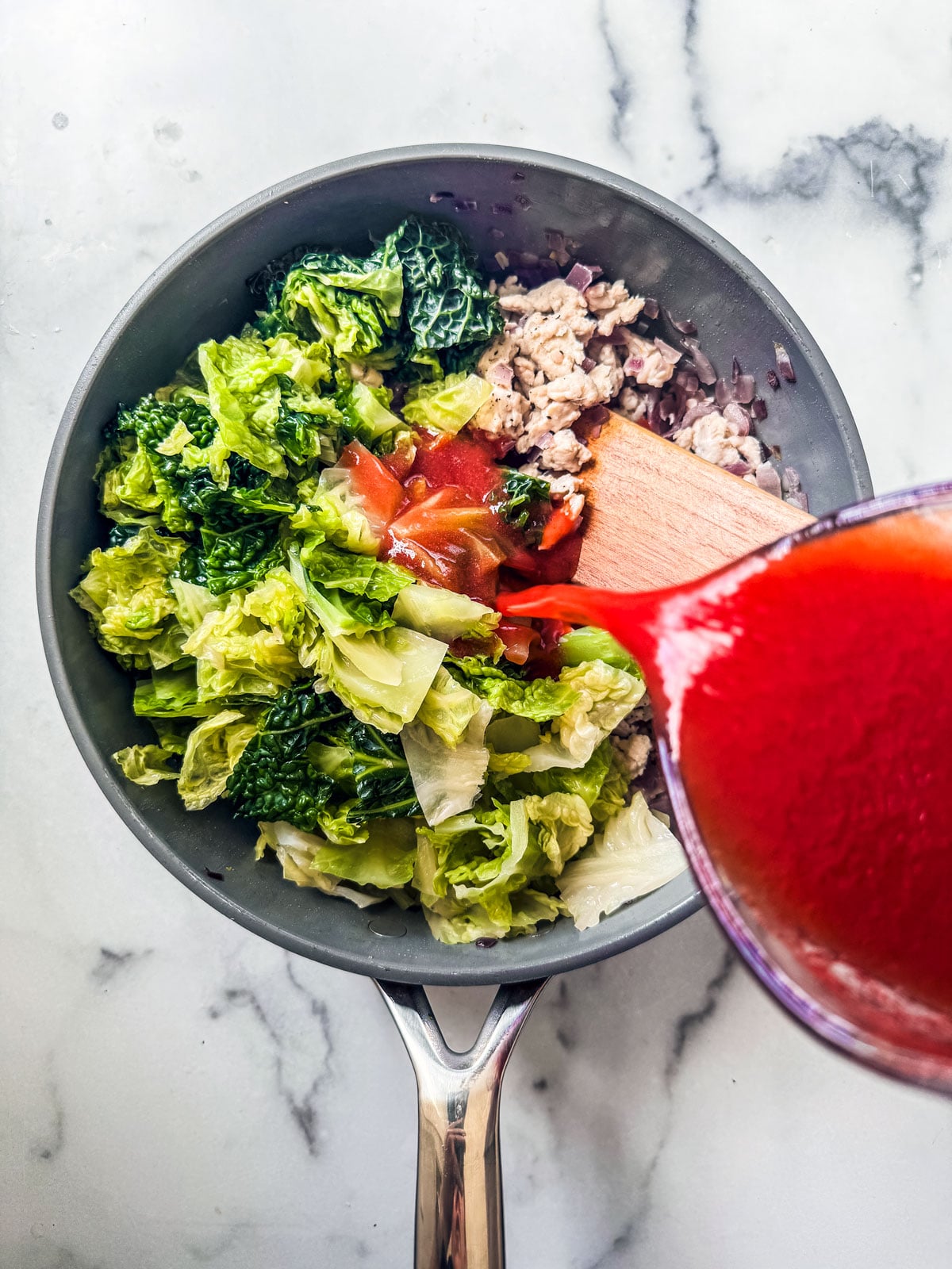 Pan with ground turkey, cabbage, and tomato juice being poured in.