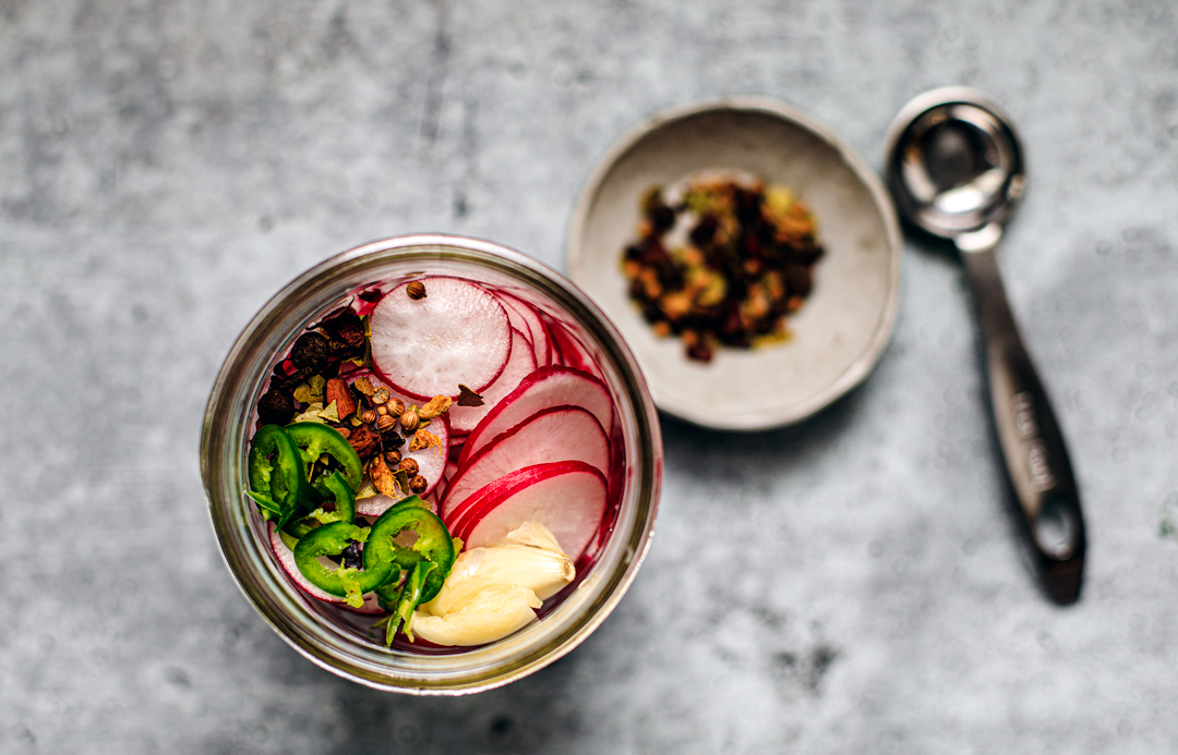 Close up of jar filled with sliced radishes, chili pepper, and spices.