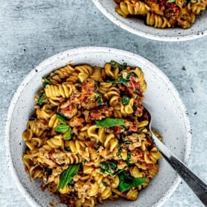 Bowls of creamy tomato rotini with ground turkey and sprigs of fresh basil as garnish.