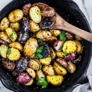 Cast iron skillet full of everything bagel seasoned roasted potatoes with fresh herbs on top.