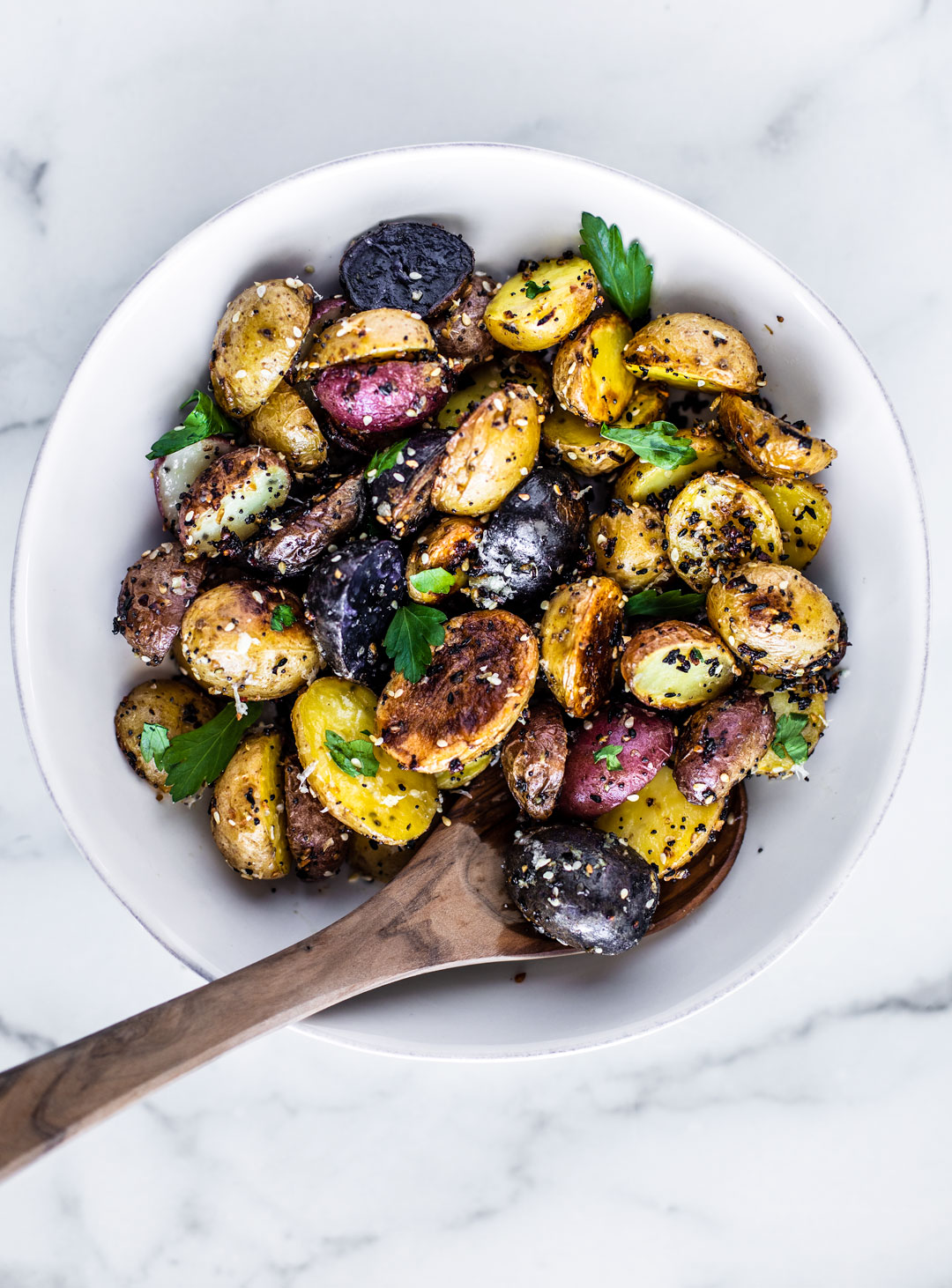 Roasted potatoes with Everything Bagel Seasoning in a white serving bowl on white marble.