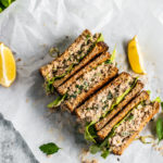 Sandwiches stacked and set down on parchment paper with lemon wedges.