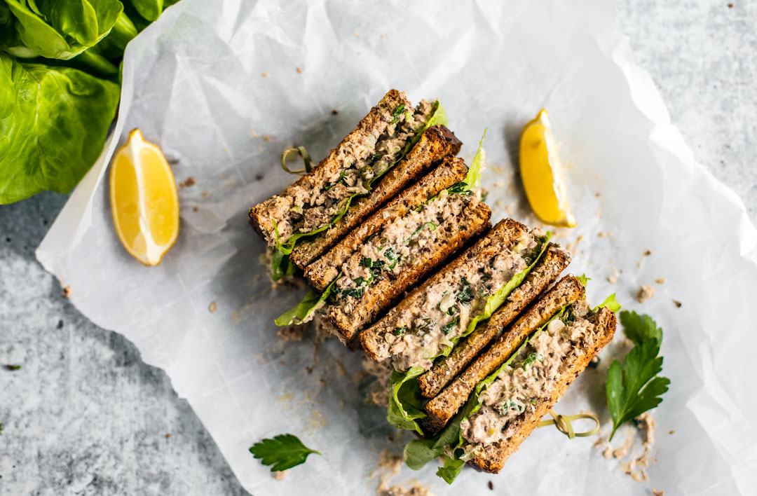 Sandwiches stacked and set down on parchment paper with lemon wedges.