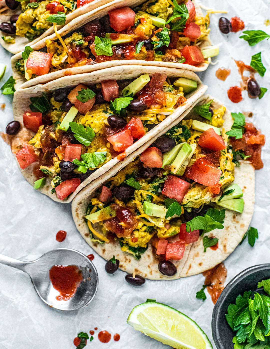 Platter of breakfast tacos stuffed with scrambled eggs, black beans, tomatoes, and drizzled with hot sauce.