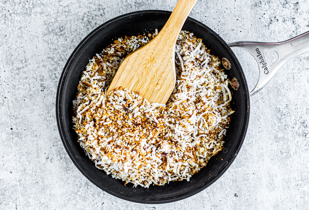 Lightly toasted shredded coconut and panko breadcrumbs in a pan with a spatula.