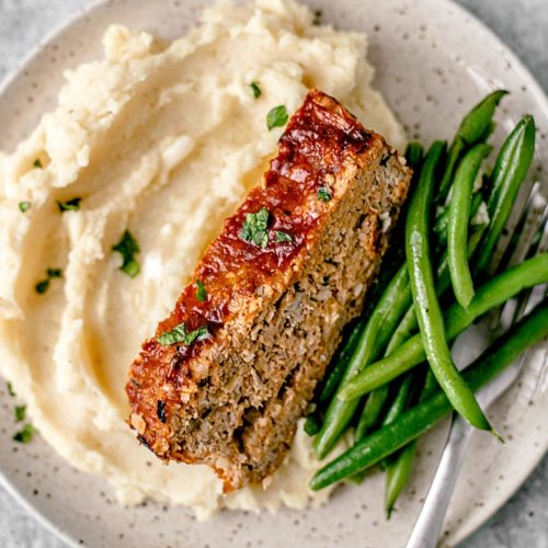 Slice of turkey meatloaf on a plate with mashed potatoes and green beans.