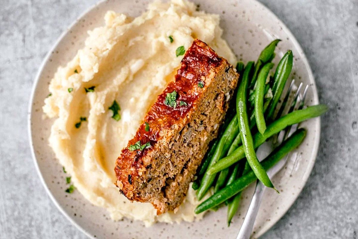 Slice of ground turkey meatloaf over mashed potatoes and green beans.