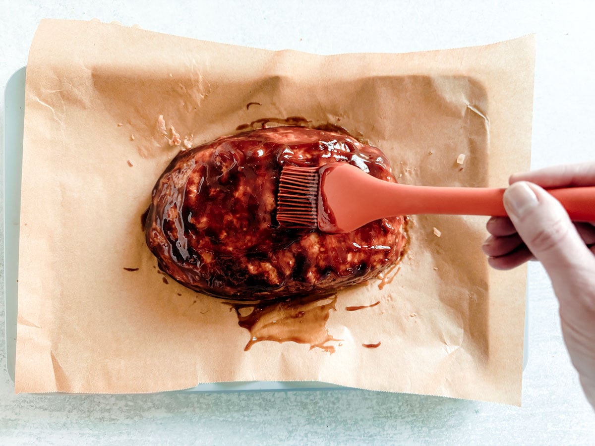 Ground turkey meatloaf being brushed with ketchup glaze.