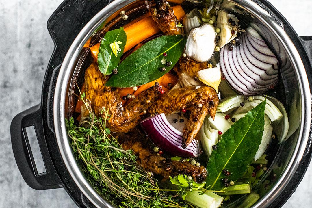 Overhead view of Instant Pot filled with water, colorful vegetable scraps, and roasted chicken scraps.