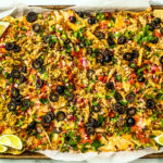 Sheet pan full of baked cheesy nachos covered in veggies and mackerel.