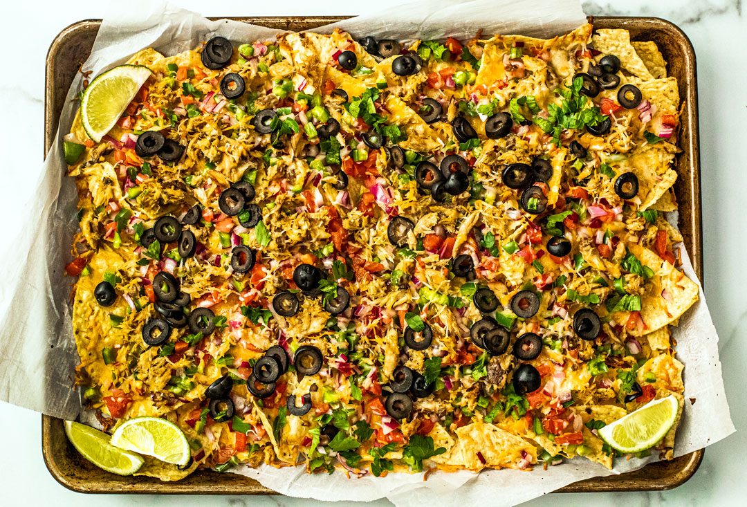 Sheet pan full of baked cheesy nachos covered in veggies and mackerel.