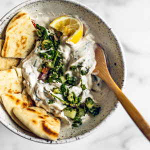 Bowl of mint Greek yogurt sauce with pitas and a squeezed lemon.