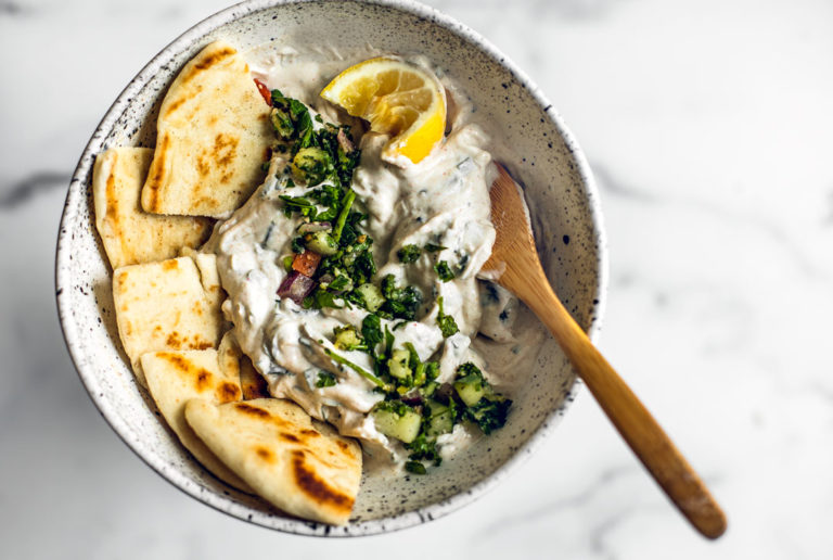 Bowl of mint Greek yogurt sauce with pitas and a squeezed lemon.