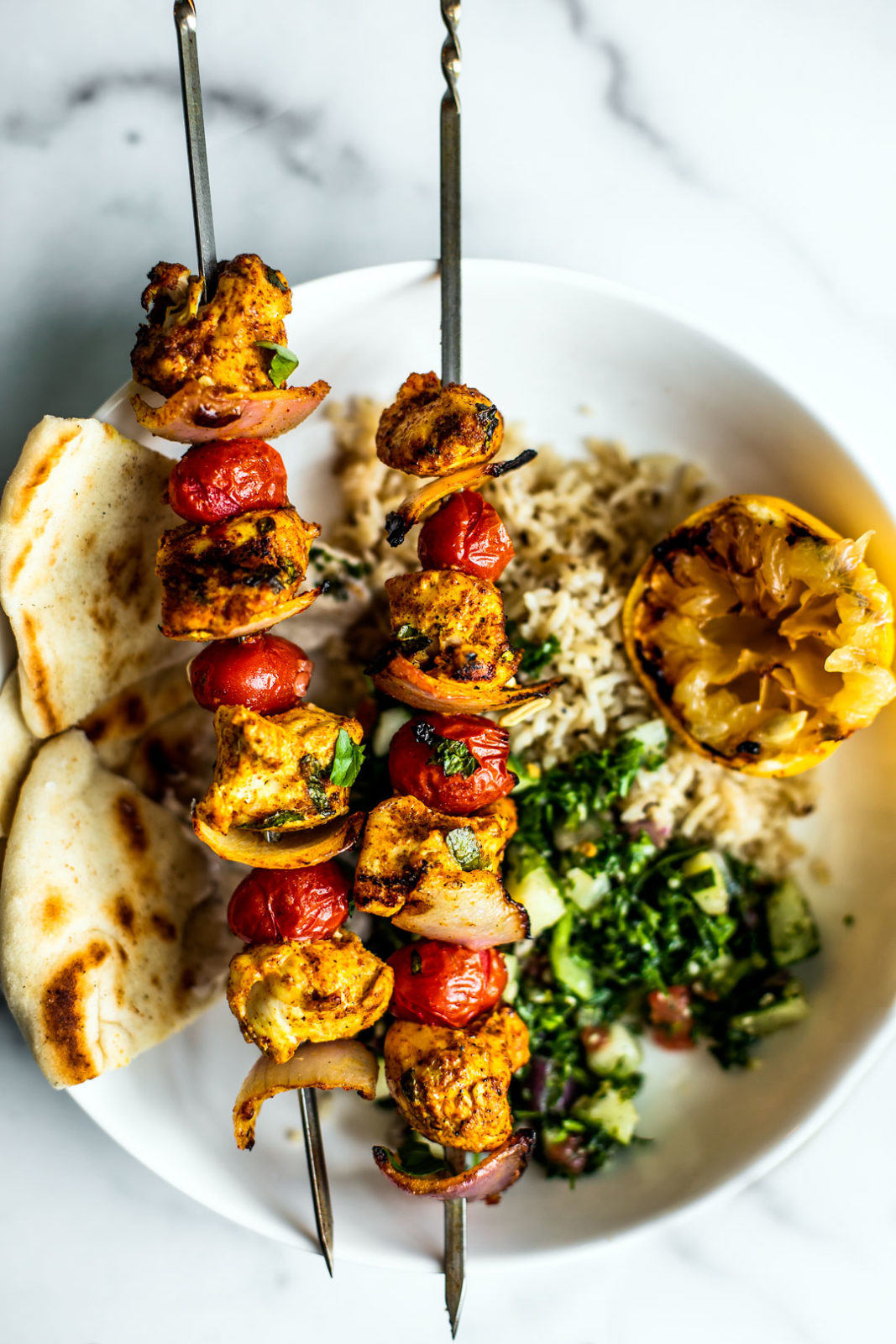 Plate of rice, tabbouleh, and pitas with grilled Moroccan chicken skewers on top.