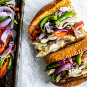 Chicken Philly Sandwich next to a sheet pan full of peppers, onions, and mushrooms.