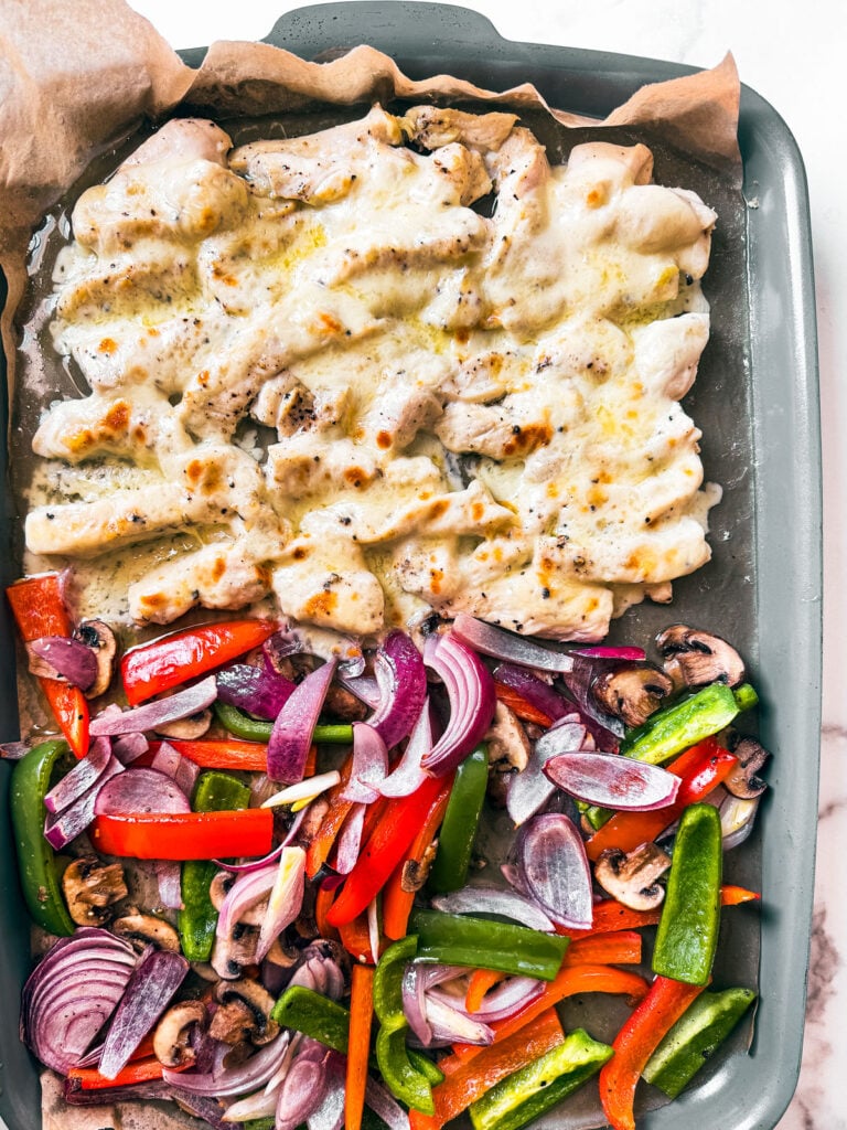 Sheet pan with veggies and cheesy chicken morsels.