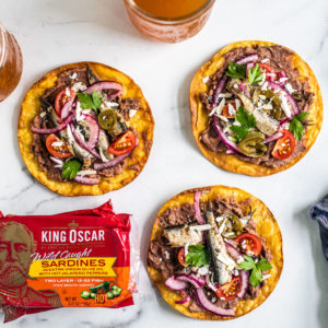 Spicy tostadas laid out around pints of beer and cans of King Oscar sardines.
