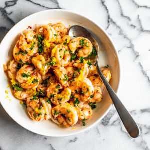 White serving bowl full of buttery shrimp garnished with fresh parsley.