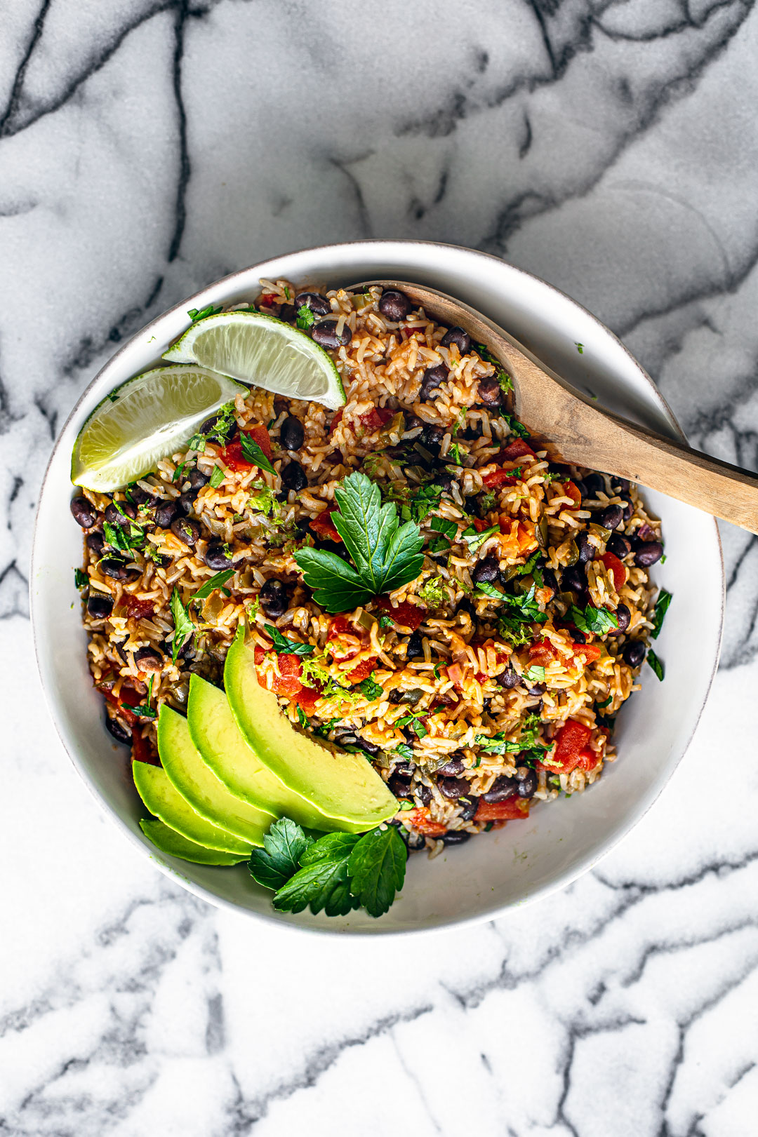 Aerial shot of serving bowl full of Instant Pot Mexican Rice garnished with fresh parsley, sliced avocado, and lime wedges.