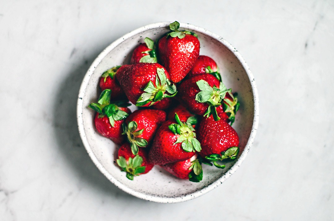 White bowl filled with juicy red strawberries.