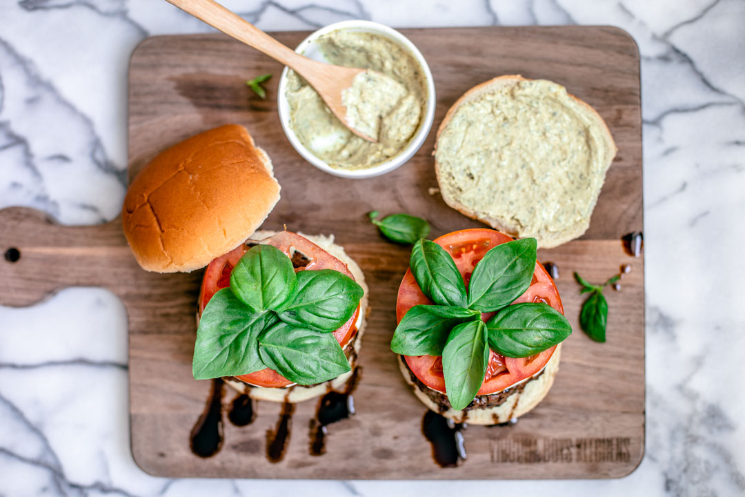 Aerial view of burgers stacked with mozzarella, tomatoes, and basil with a side of pesto mayo.