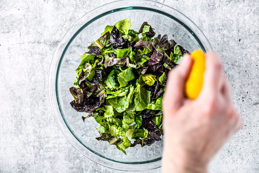 Hand squeezing lemon juice over a bowl of chopped lettuce.