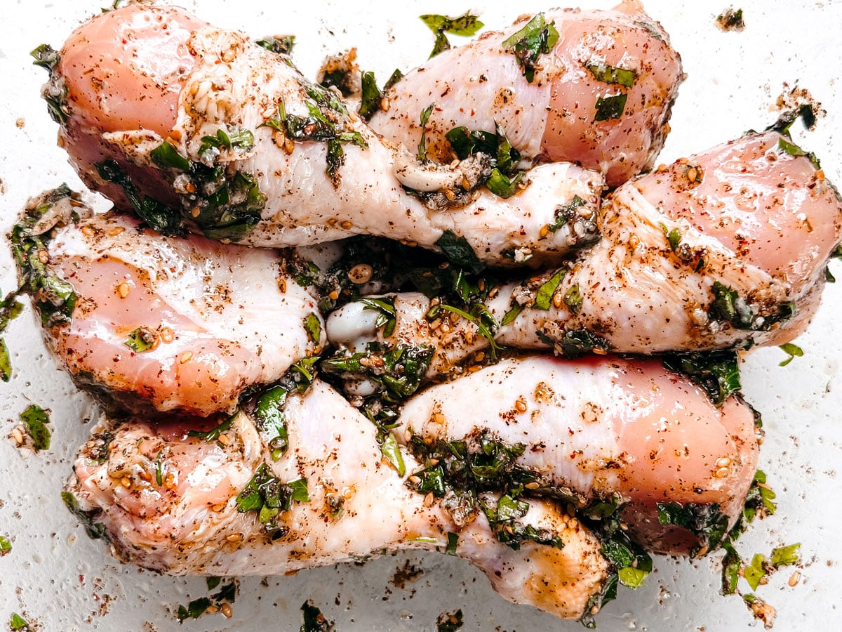Uncooked chicken drumsticks are tossed in marinated in a mixing bowl.