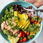 Colorful bowl of flaked tuna with vegetables and an herb dressing drizzled on top.