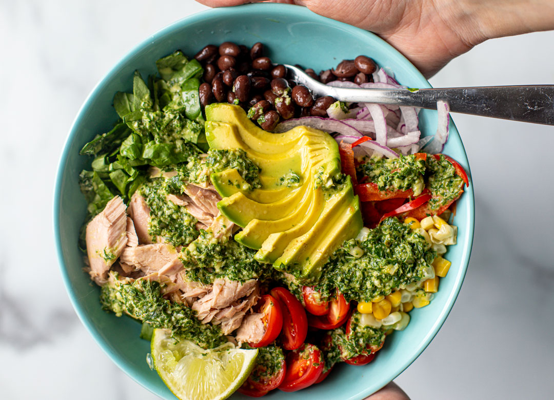 Colorful bowl of flaked tuna with vegetables and an herb dressing drizzled on top.