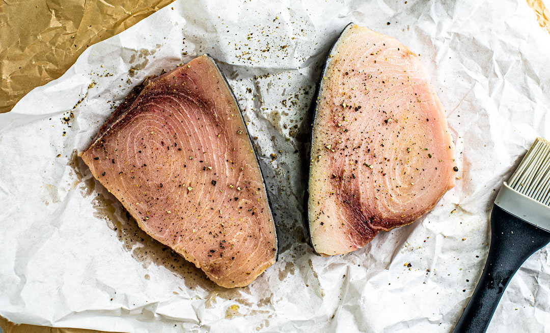 Raw swordfish on parchment, seasoned with salt and pepper.