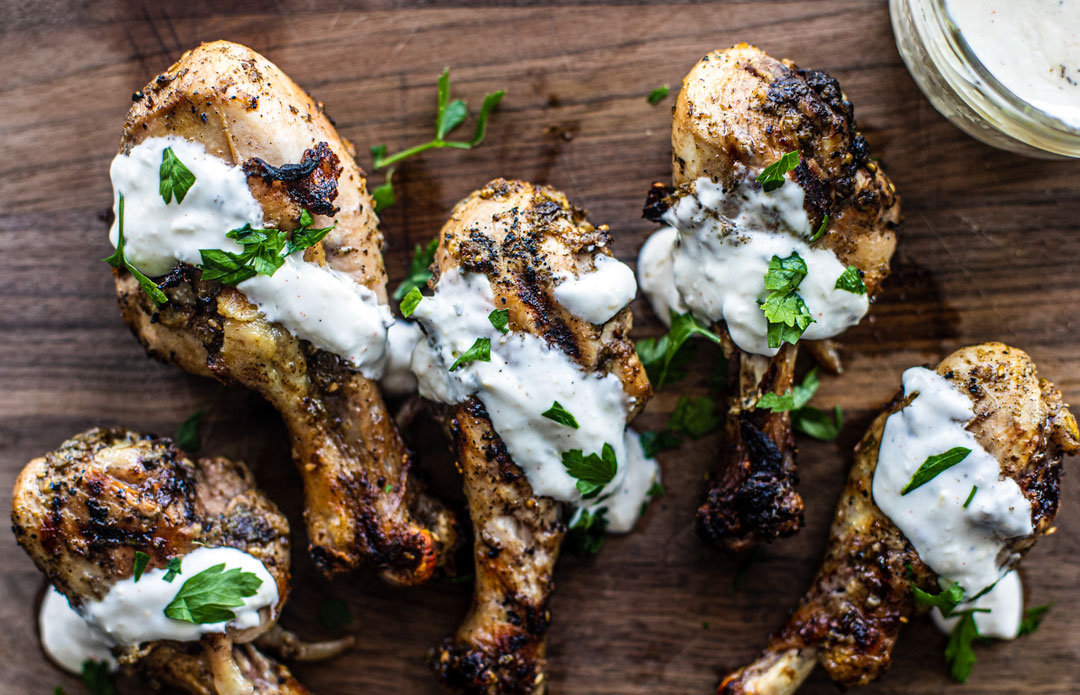 Chicken drumsticks spread out on wooden cutting board with lemon yogurt drizzle.