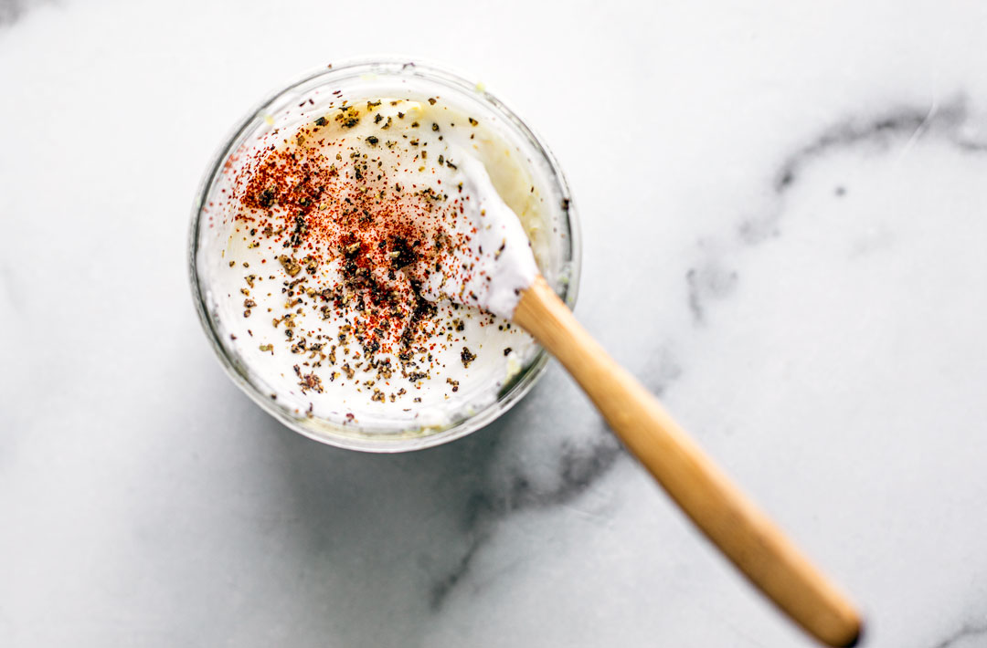 Small jar of lemon yogurt sauce sprinkled with cracked pepper and paprika.