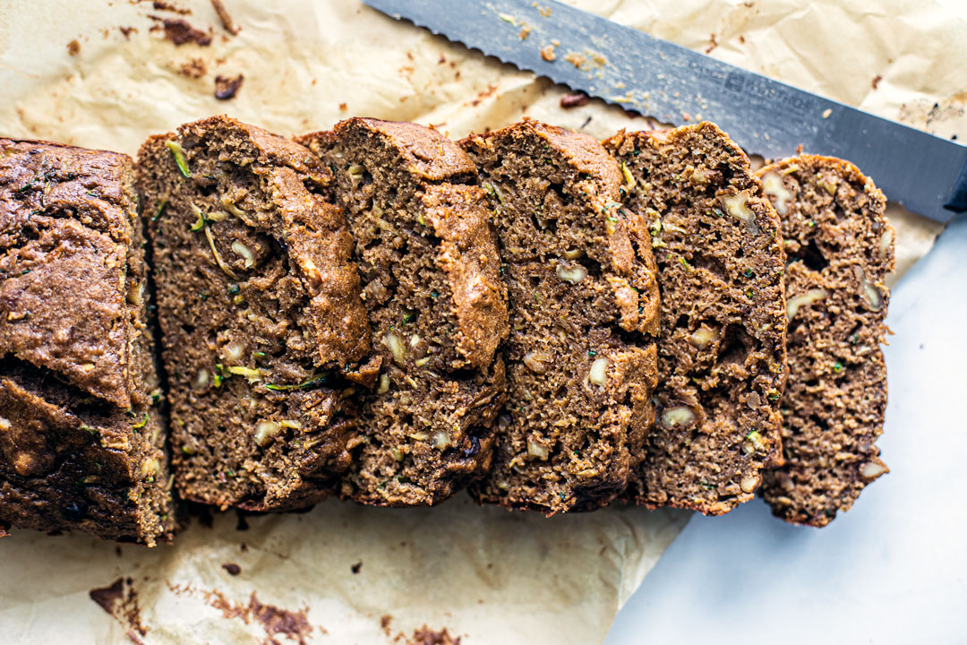 Zucchini bread slices lined up with a bread knife.