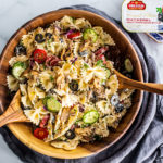 Greek pasta tossed in a bamboo bowl with serving spoons.