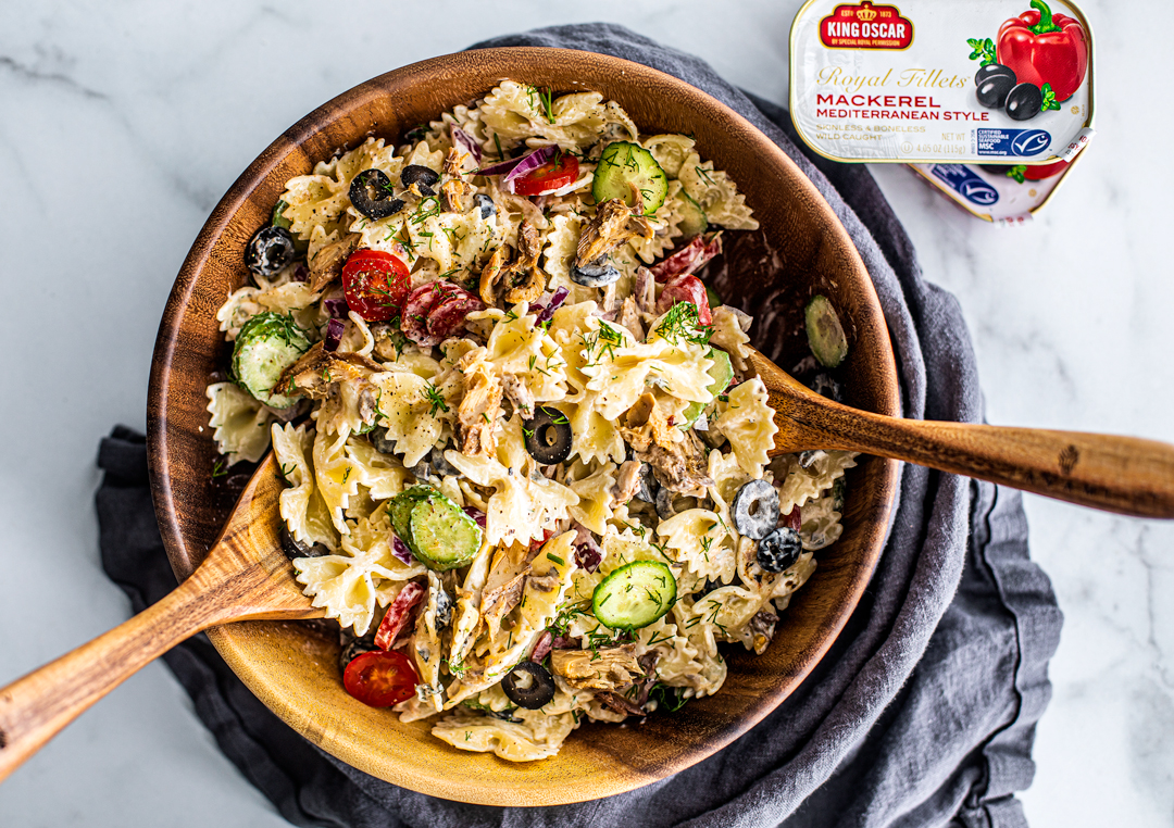 Greek pasta tossed in a bamboo bowl with serving spoons.