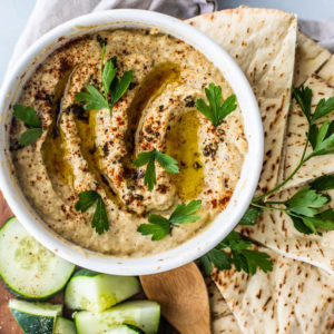 Close up of homemade baba ganoush in bowl with platter of pita and cucumbers.