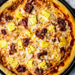 Cooked Hawaiian pizza on cast iron pizza pan.