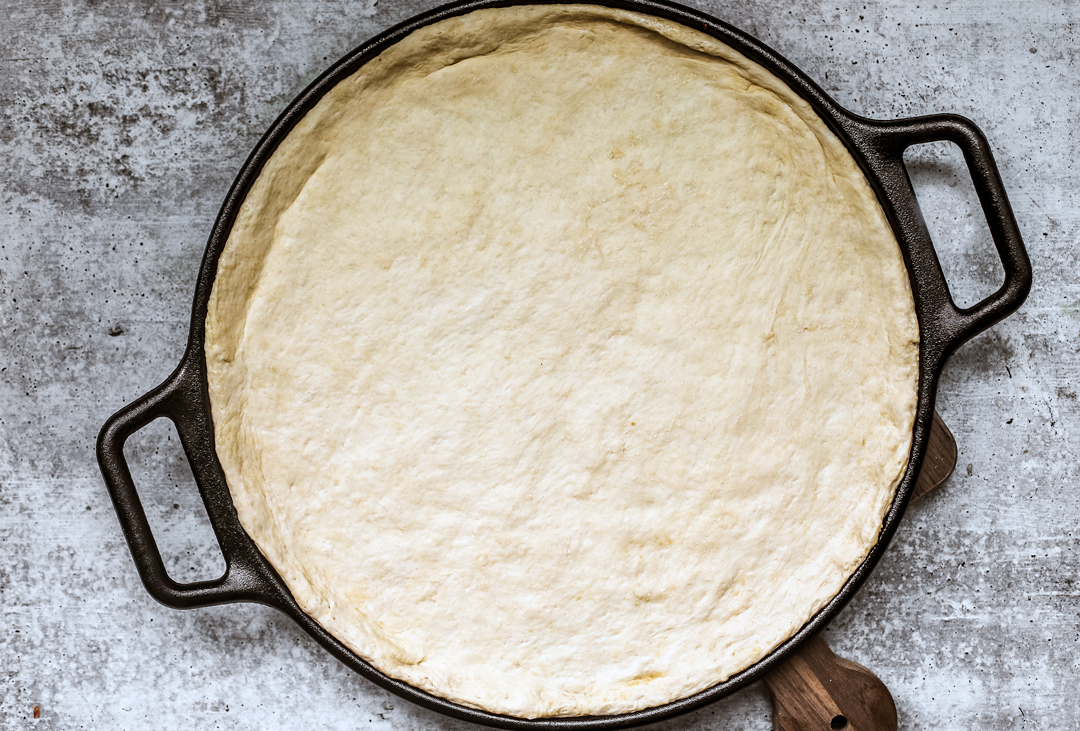 Raw pizza dough spread out onto a cast iron pizza pan.