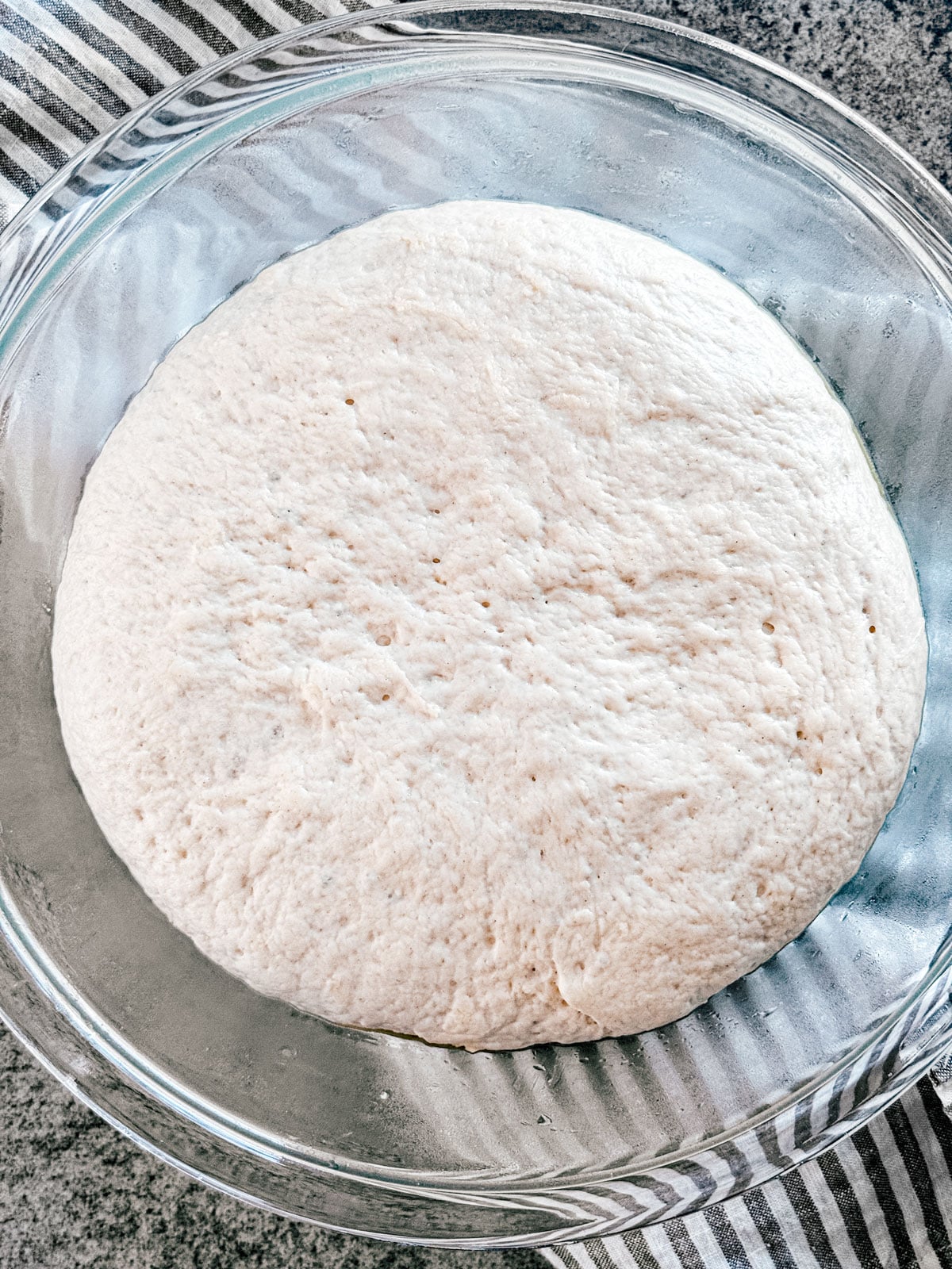 Risen pizza dough in a glass mixing bowl.
