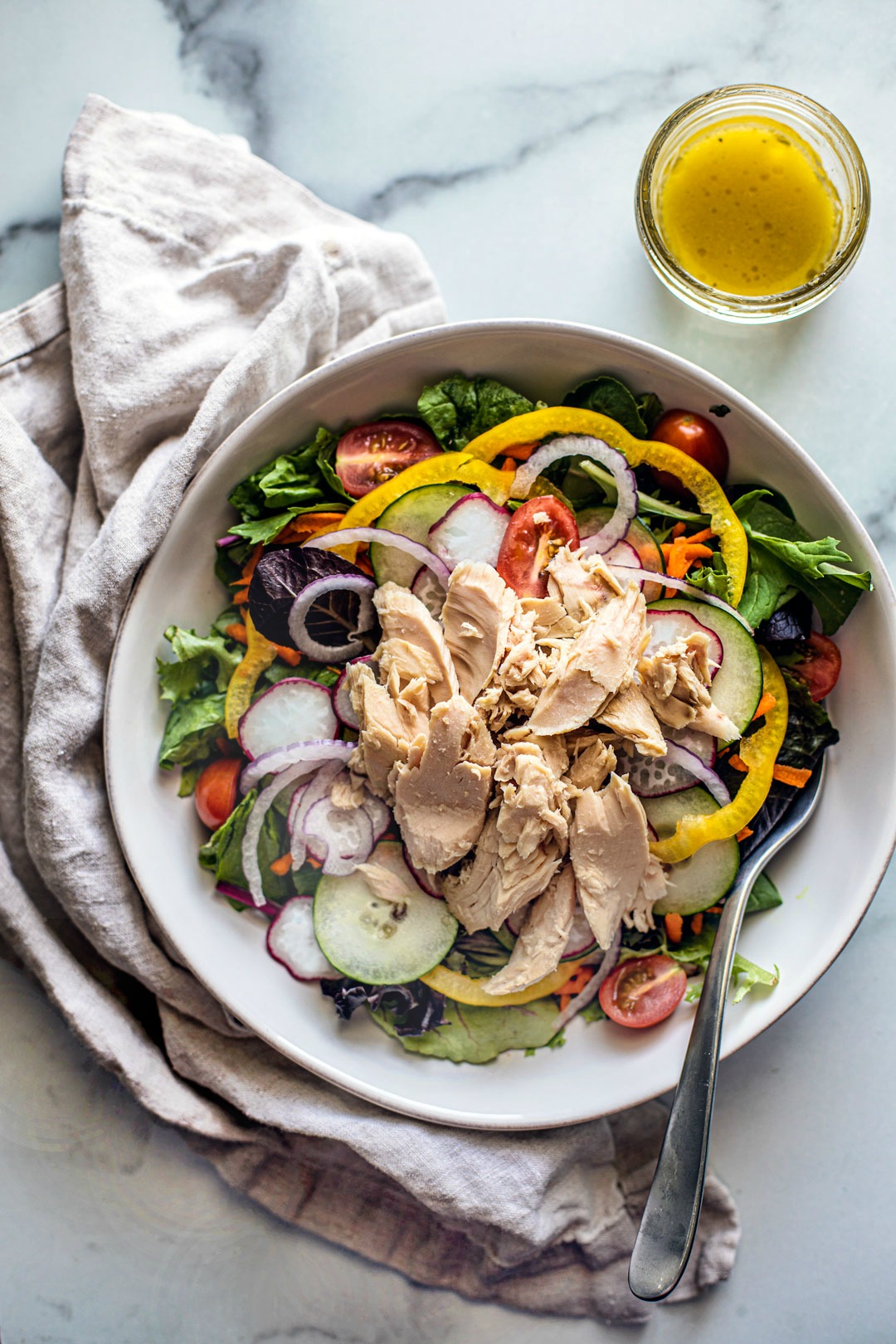 Overhead shot of seasonal vegetable salad topped with big chunks of tuna; homemade dressing on the side.