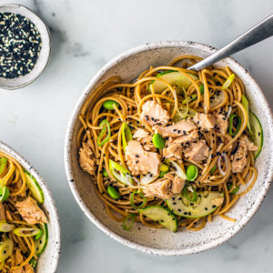 Soba noodles in a bowl with salmon, edamame, cucumbers, and scallions.