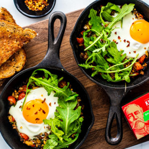 Two miniature skillets filled with Fisherman's Eggs and topped with arugula.
